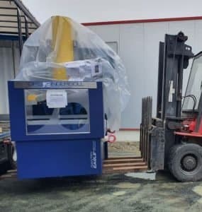 Forklift transporting an OPS Ingersoll machine wrapped in plastic outside an industrial building.
