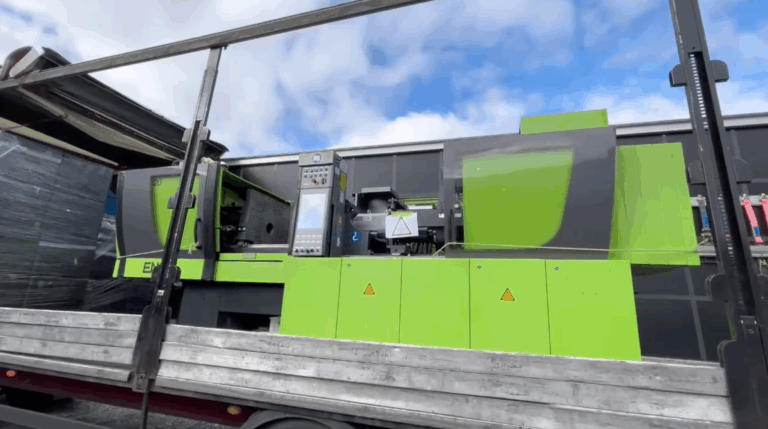 Grüne Spritzgießmaschine Abmusterung auf LKW verladen unter blauem Himmel.