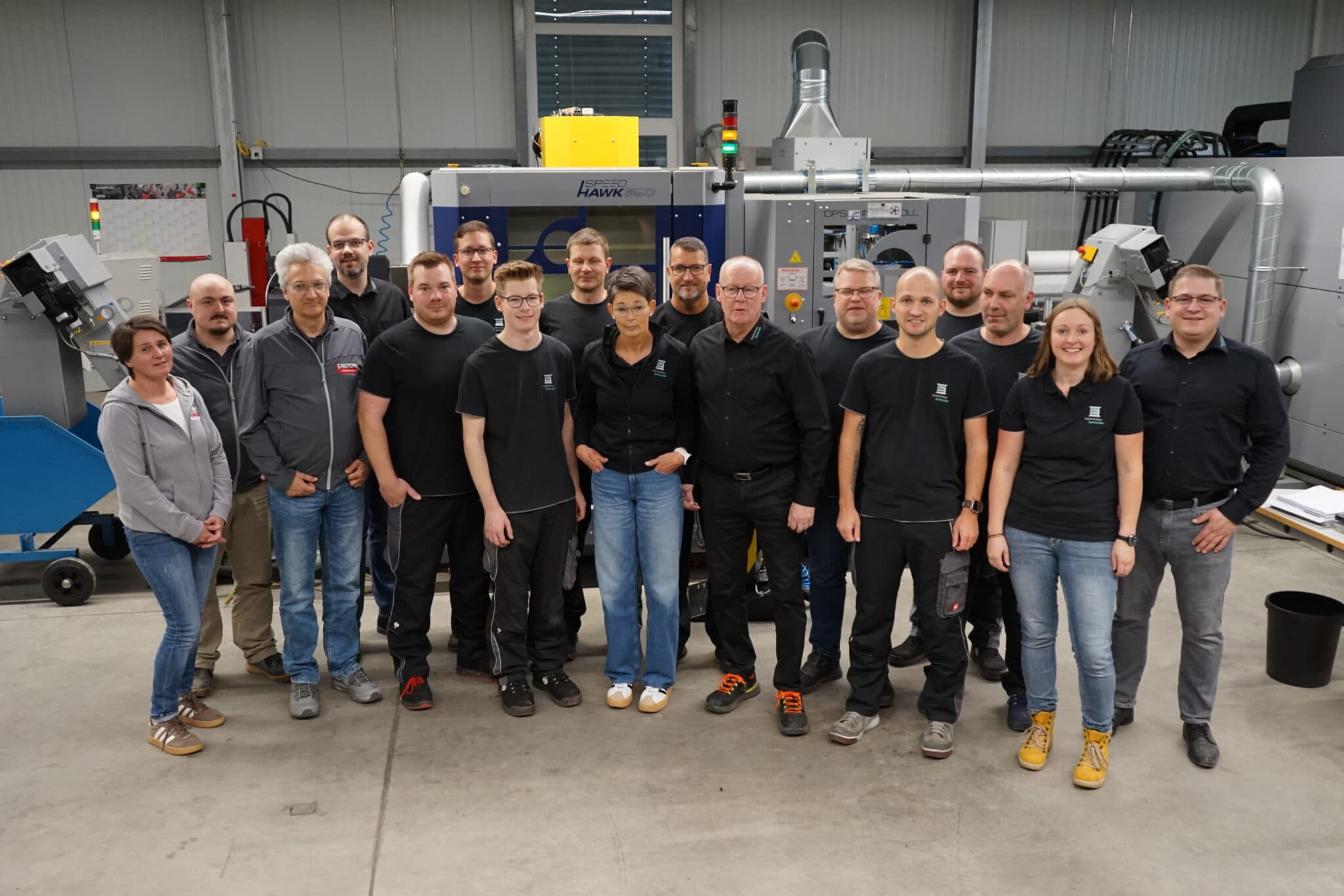 Gruppe von Mitarbeitern vor industrieller Maschine in einer Fabrikhalle.