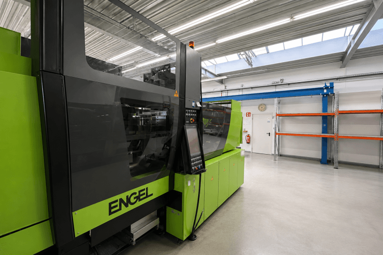 Grüne Spritzgussmaschine in moderner Industriehalle mit Regalen und Deckenbeleuchtung.