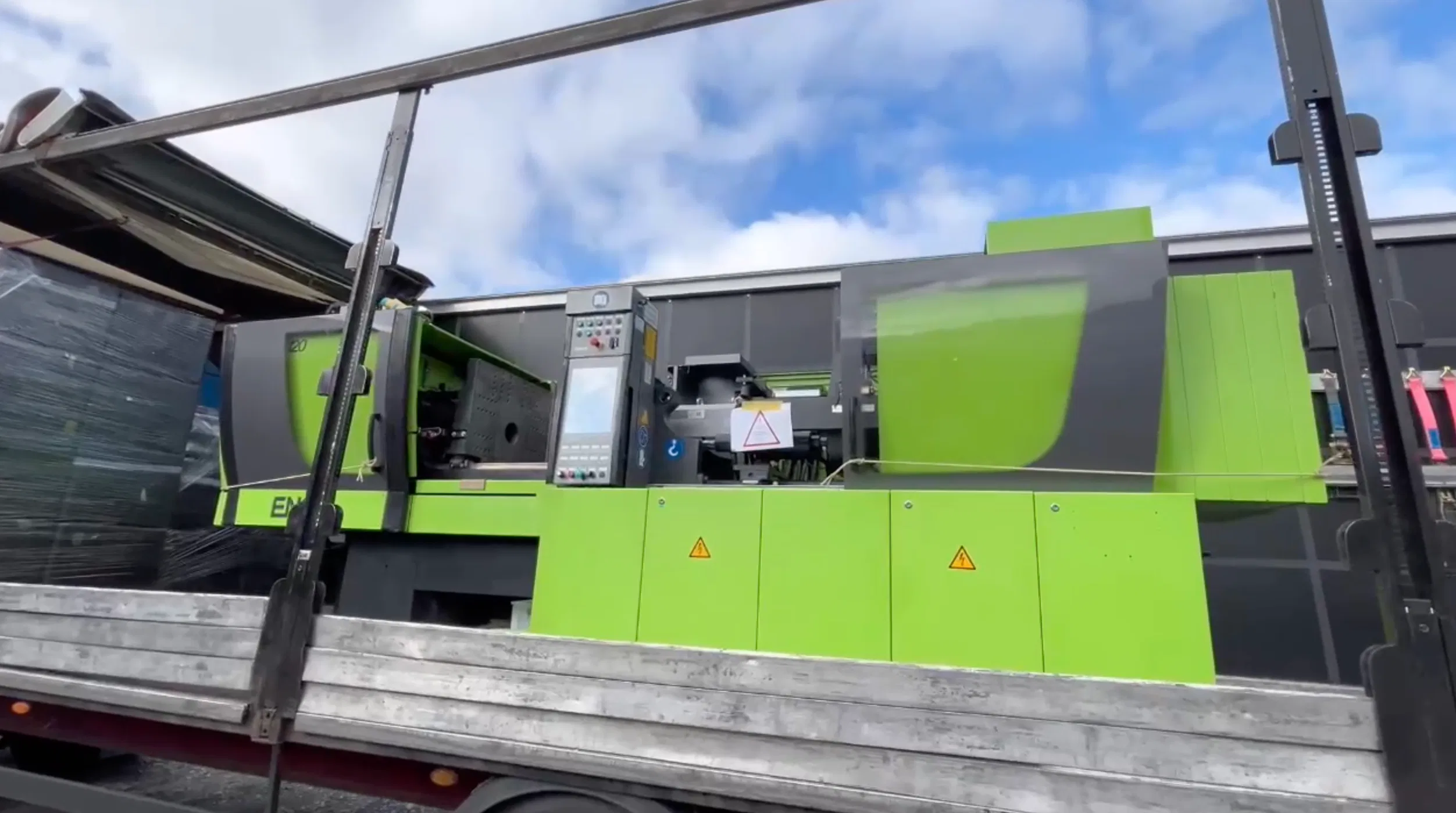 Grüne Spritzgießmaschine Abmusterung auf LKW verladen unter blauem Himmel.