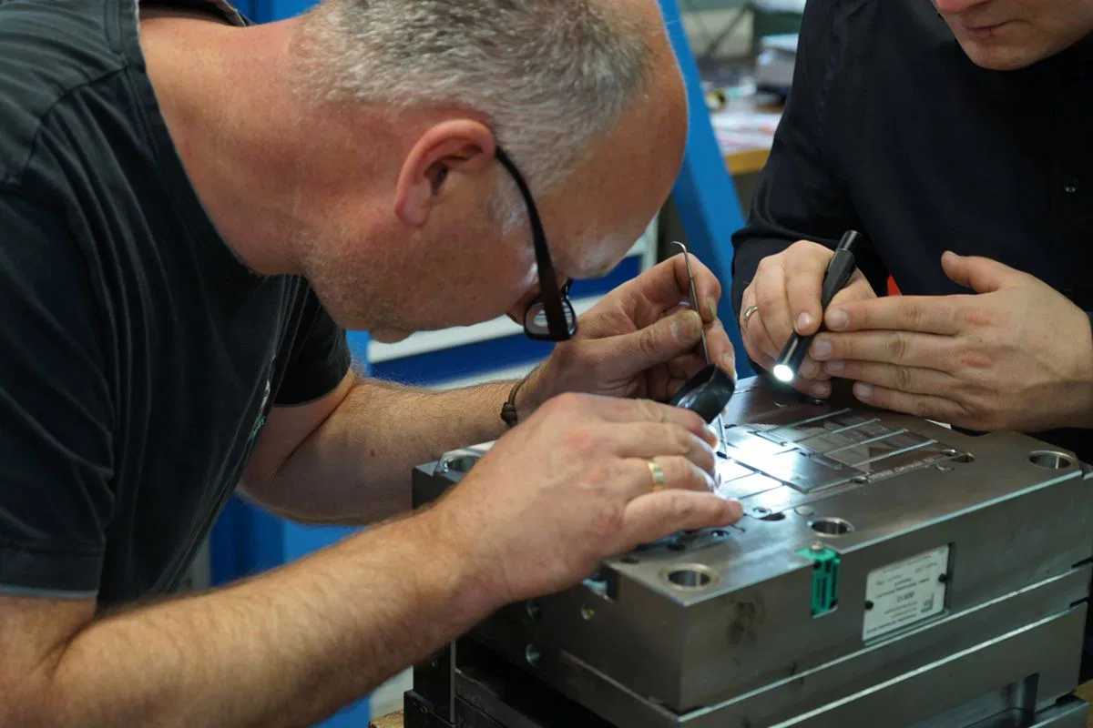 Zwei Männer inspizieren präzise Metallarbeit mit Taschenlampen in Werkstatt.